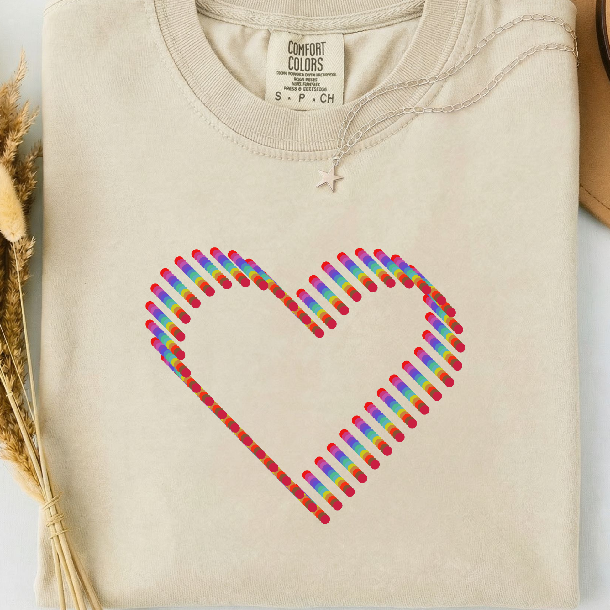 Beige comfort colors t-shirt with a colorful rainbow heart design. 