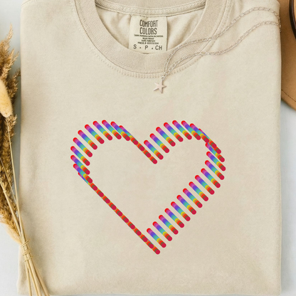 Beige comfort colors t-shirt with a colorful rainbow heart design. 