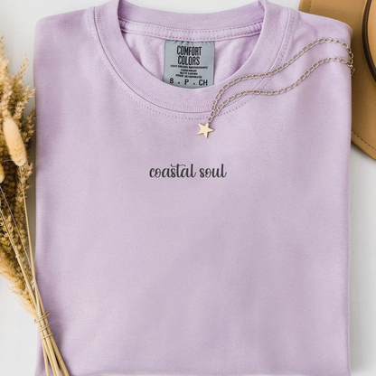 orchid comfort colors t-shirt with a back graphic design of a sun, palm trees, beach and a hammock and minimalist text on the front 'Coastal Soul'. 