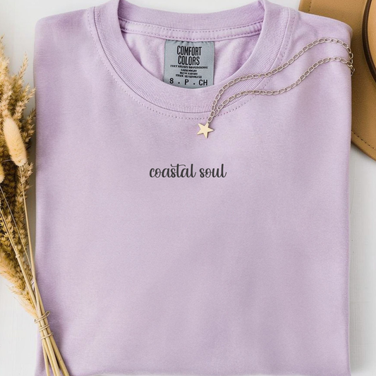 orchid comfort colors t-shirt with a back graphic design of a sun, palm trees, beach and a hammock and minimalist text on the front 'Coastal Soul'. 